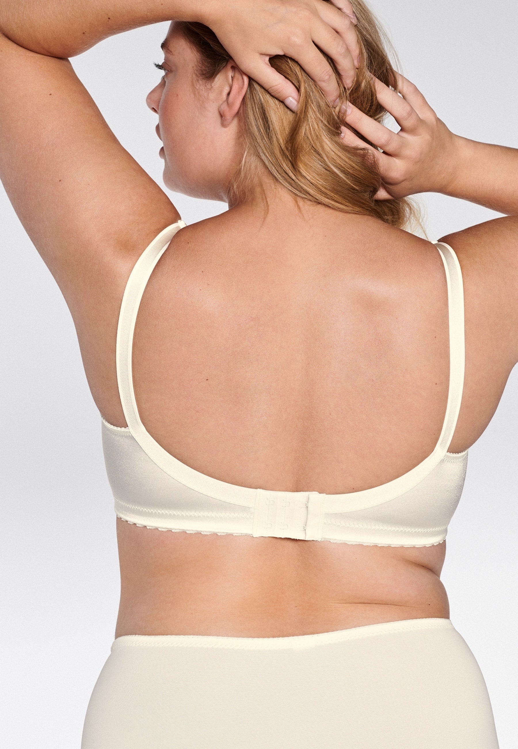 Achterzijde van vrouw die de minimizer bh met glanzend effect in de kleur ivoor van het merk Naturana draagt