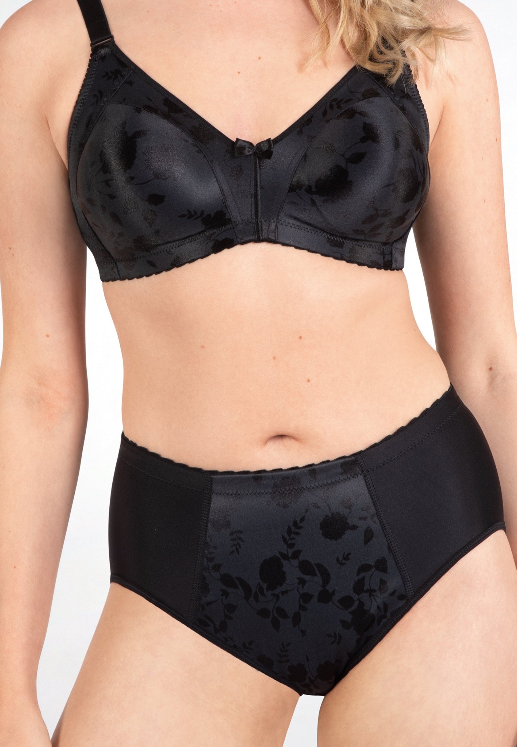 Voorzijde van vrouw die de minimizer bh en minimizer slip met bloemenpatroon in de kleur zwart van het merk Naturana draagt