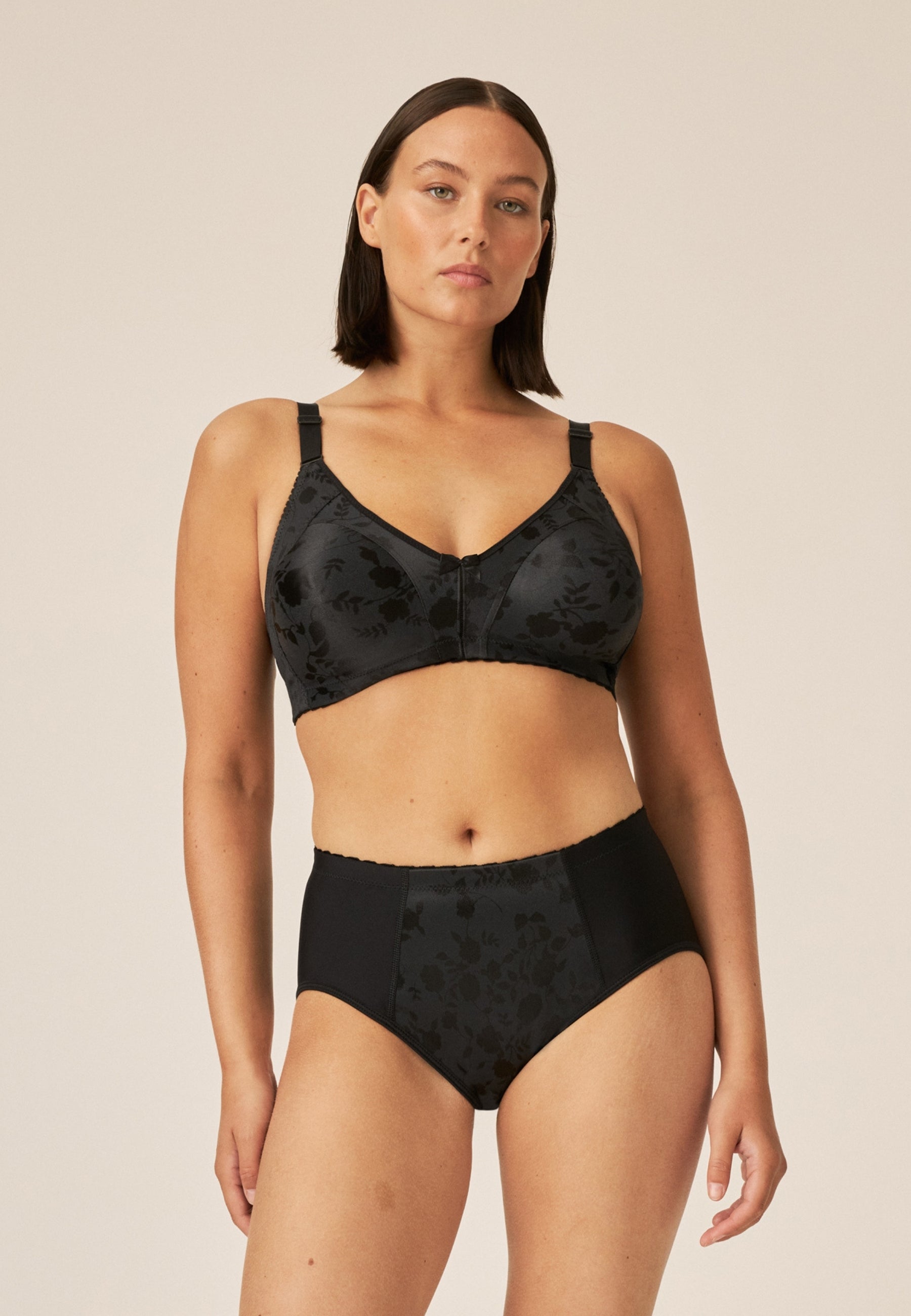 Voorzijde van vrouw die de minimizer bh en minimizer slip met bloemenpatroon in de kleur zwart van het merk Naturana draagt