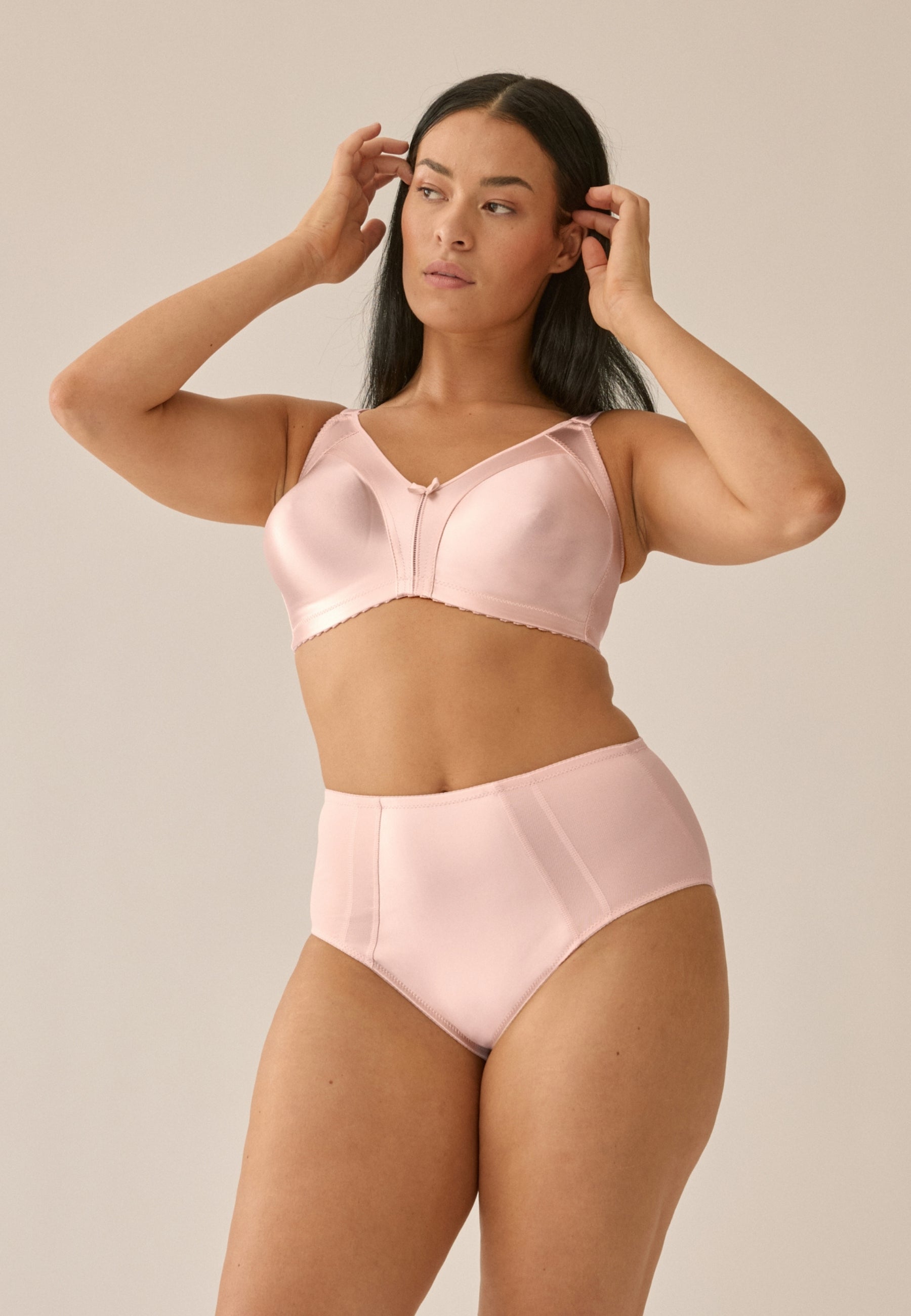 Voorzijde van vrouw die de minimizer bh en minimizer slip met glanzend effect in de kleur blush van het merk Naturana draagt