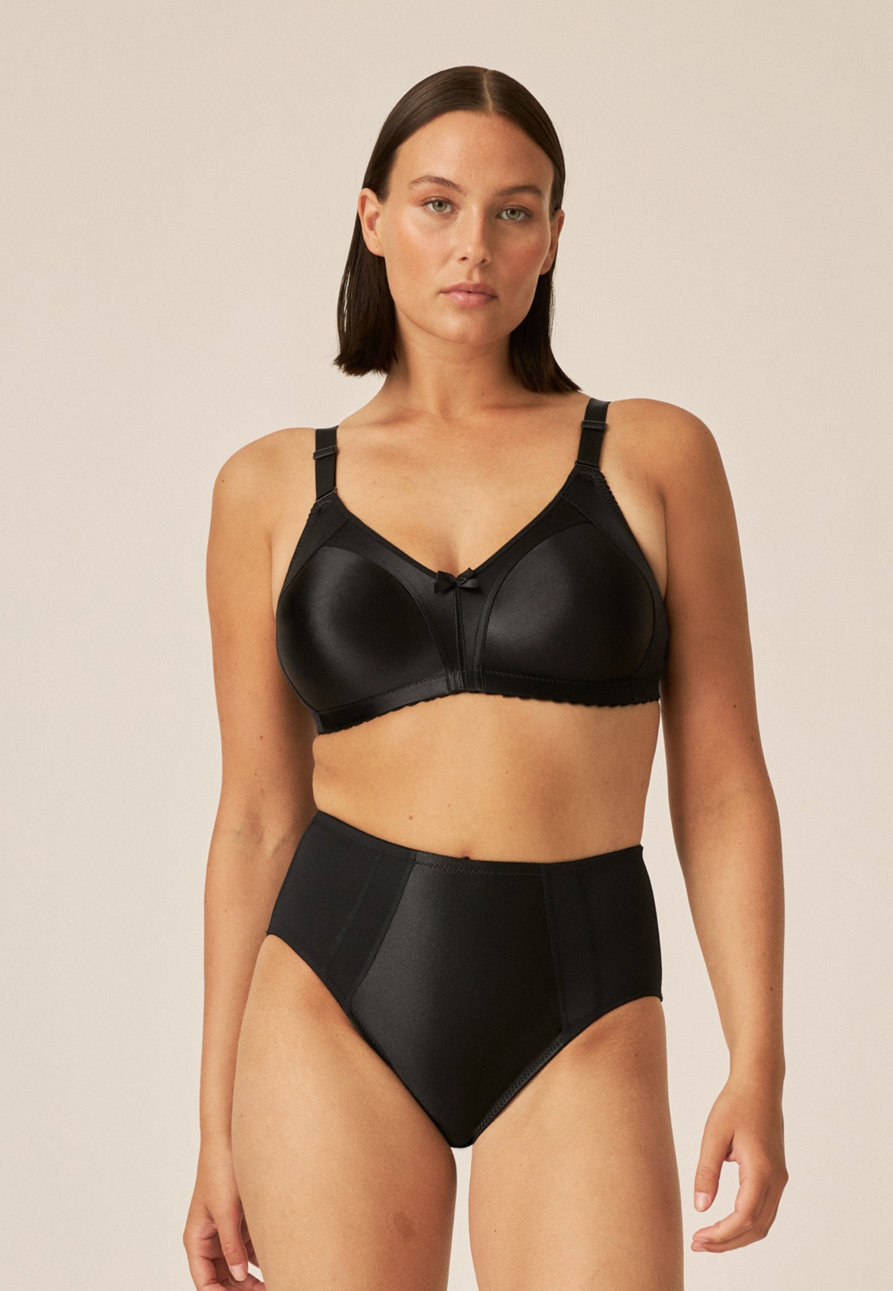 Voorzijde van vrouw die de minimizer bh en minimizer slip met glanzend effect in de kleur zwart van het merk Naturana draagt