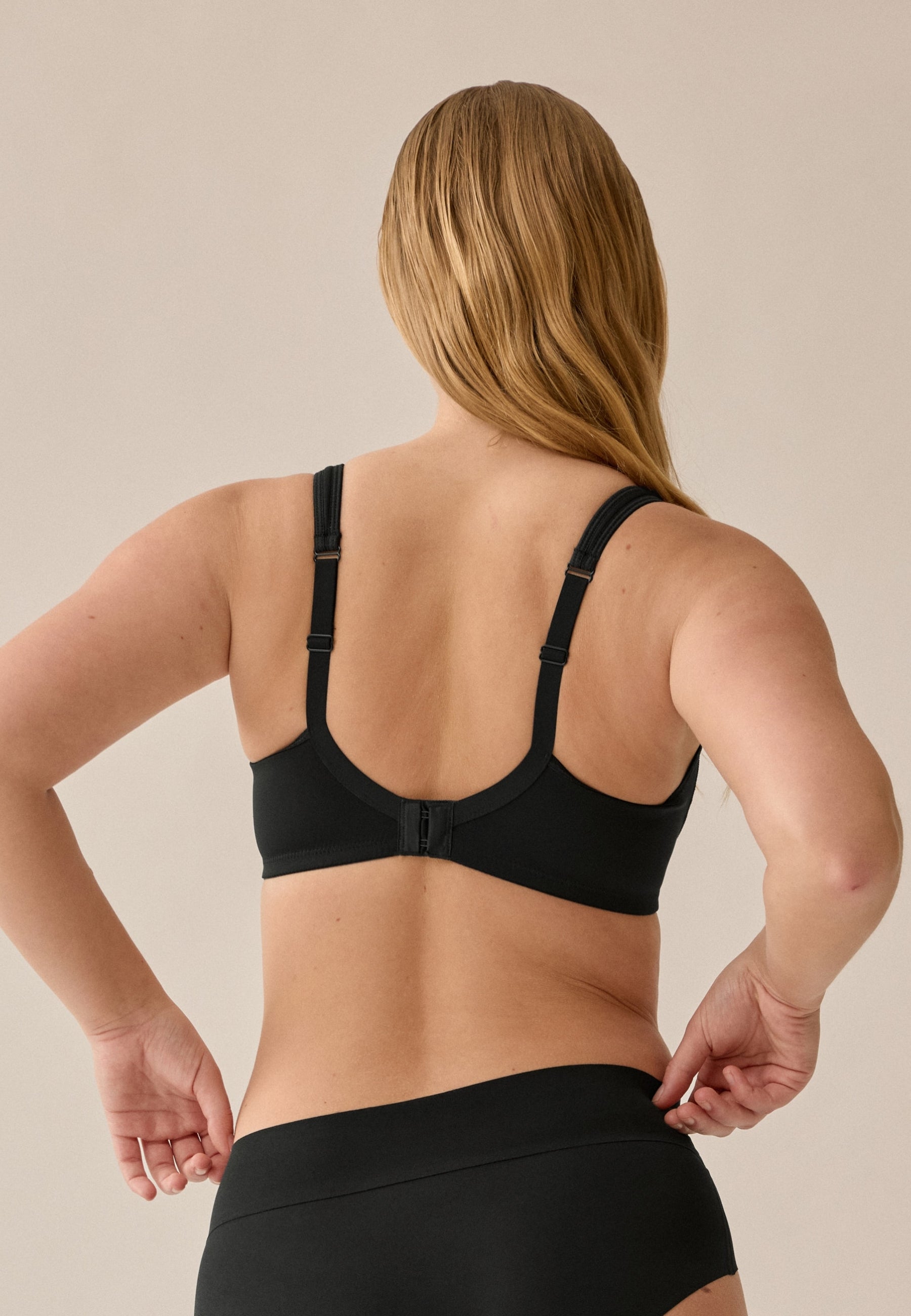 Achterzijde van vrouw die de soft bh met meshrand in de kleur zwart van het merk Naturana draagt