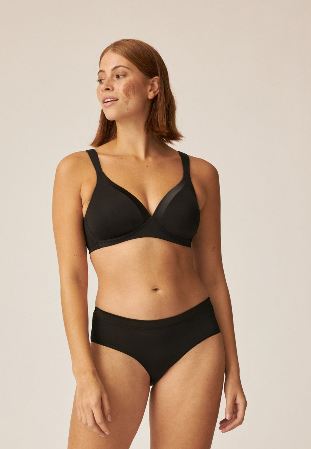 Voorzijde van vrouw die de soft bh met glansband en slip met glansband in de kleur zwart van het merk Naturana draagt