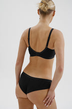 Achterzijde van vrouw die de lambada prothese bh en de lambade slip in de kleur zwart van het merk Megami draagt