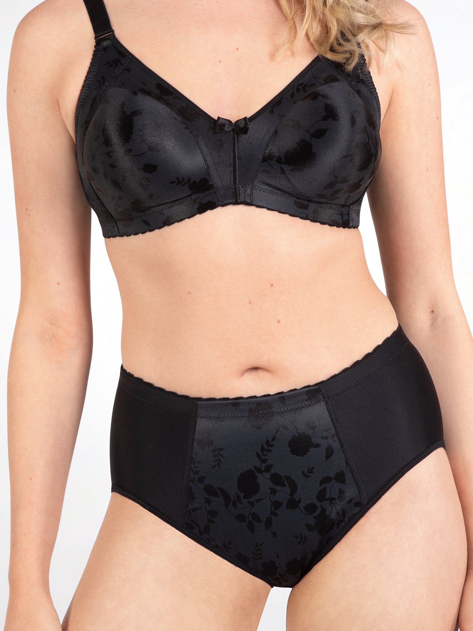 Voorzijde van vrouw die de minimizer bh met bloemenpatroon en slip met bloemenpatroon in de kleur zwart van het merk Naturana draagt
