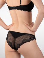Achterzijde van vrouw die de tanga met kant en soft bh met kant in de kleur zwart van het merk Naturana draagt