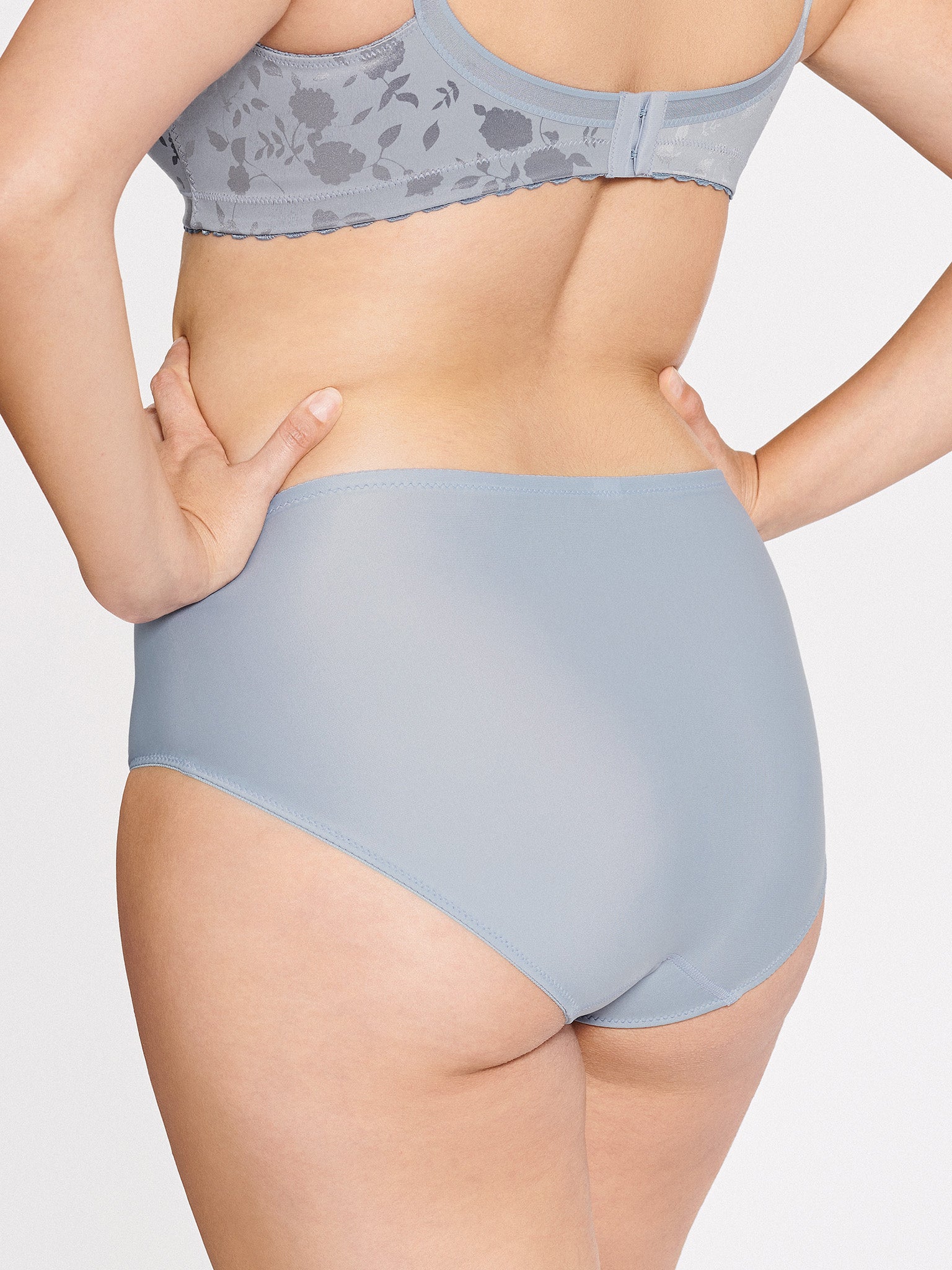 Achterzijde van vrouw die de minimizer slip met bloemenpatroon in de kleur raindrops van het merk Naturana draagt