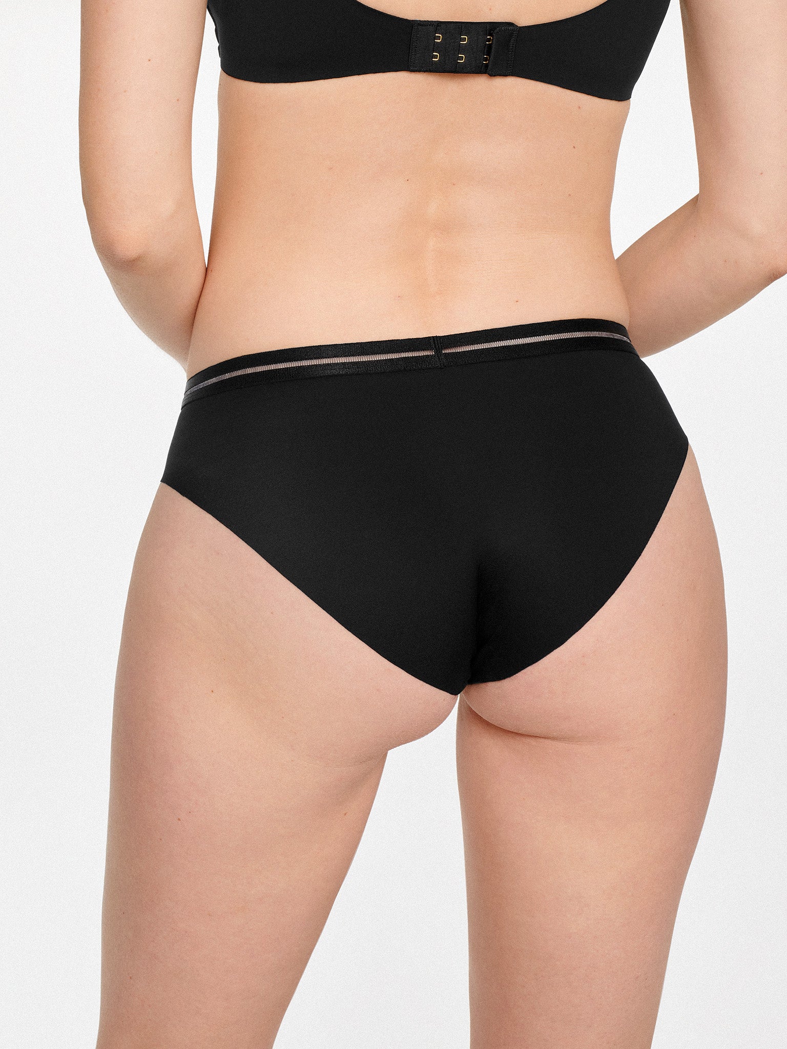 Achterzijde van vrouw die de slip met mesh detail in de kleur zwart van het merk Naturana draagt