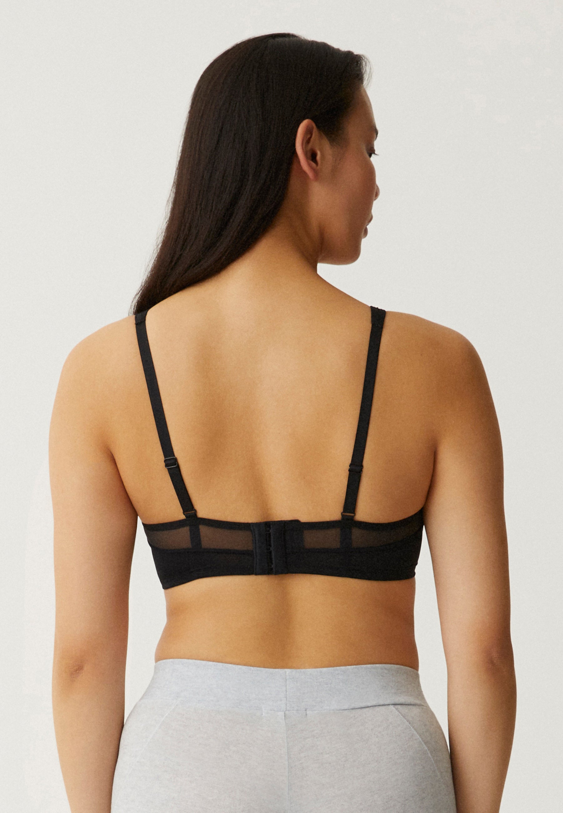 Achterzijde van vrouw die de soft bh met mesh bandjes in de kleur zwart van het merk Naturana draagt