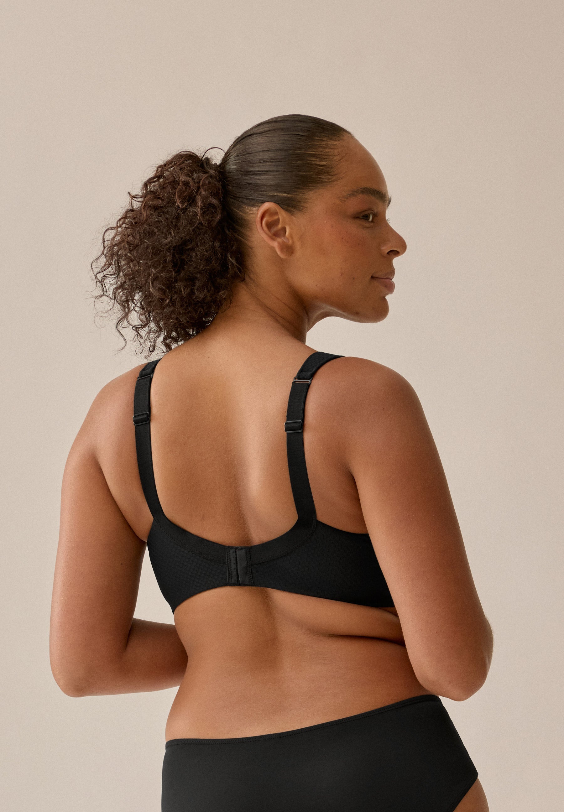 Achterzijde van vrouw die de soft bh met glansband in de kleur zwart van het merk Naturana draagt