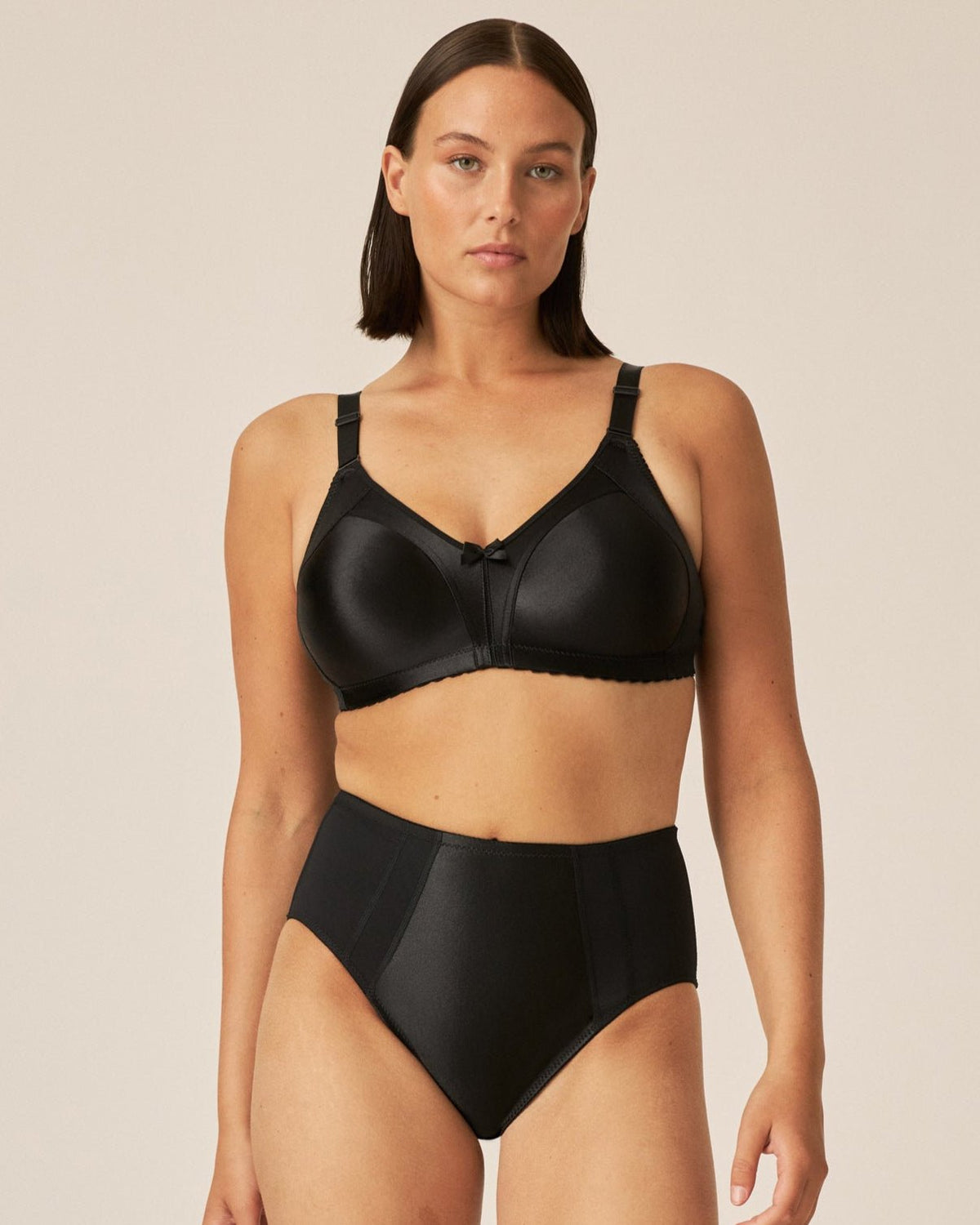 Voorzijde van vrouw die de minimizer bh met glanzend patroon in de kleur zwart van het merk Naturana draagt