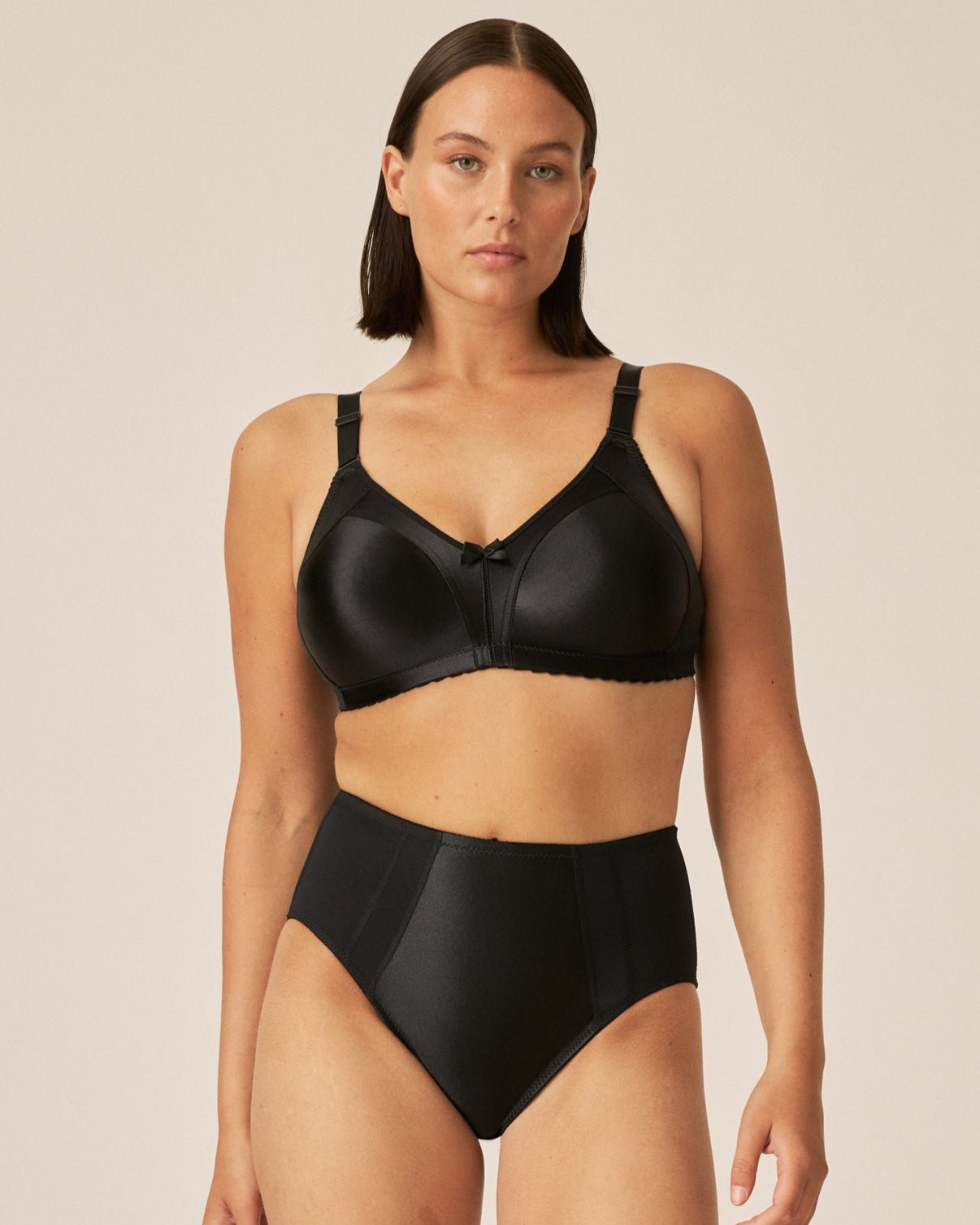 Voorzijde van vrouw die de minimizer bh met glanzend patroon in de kleur zwart van het merk Naturana draagt