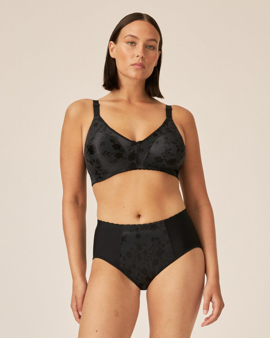 Voorzijde van vrouw die de minimizer bh met bloemenpatroon en slip met bloemenpatroon in de kleur zwart van het merk Naturana draagt