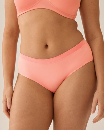 Voorzijde van vrouw die de soft bh met glansband en slip met glansband in de kleur peach pink van het merk Naturana draagt