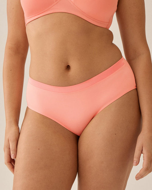 Voorzijde van vrouw die de soft bh met glansband en slip met glansband in de kleur peach pink van het merk Naturana draagt