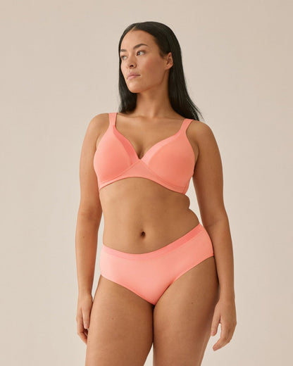 Voorzijde van vrouw die de soft bh met glansband en slip met glansband in de kleur peach pink van het merk Naturana draagt