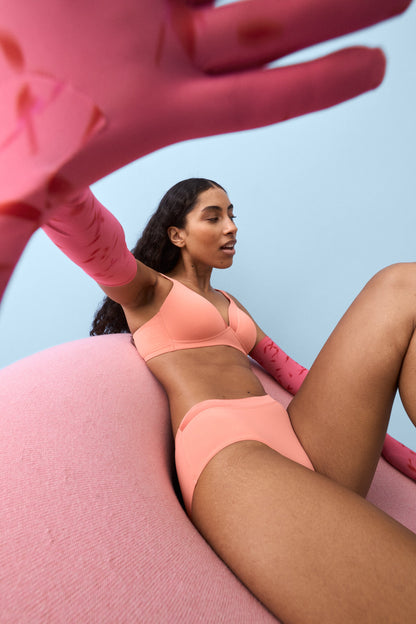 Voorzijde van vrouw die de soft bh met glansband en slip met glansband in de kleur peach pink van het merk Naturana draagt