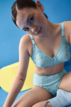 Voorzijde van vrouw die de minimizer bh met bloemenpatroon en slip met bloemenpatroon in de kleur Aquamarine van het merk Naturana draagt