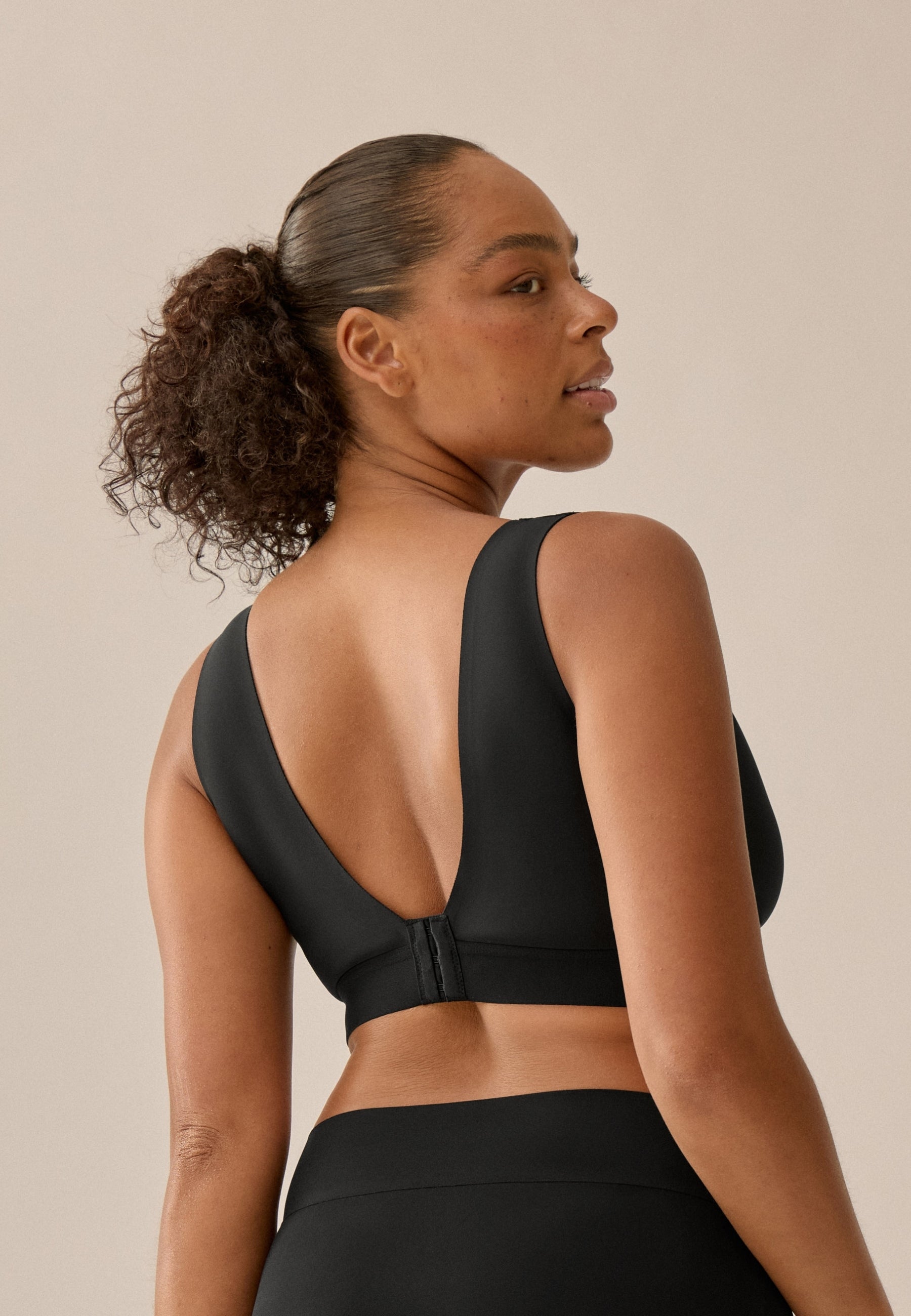 Achterzijde  van vrouw die de back smoother bh in de kleur zwart van het merk Naturana draagt