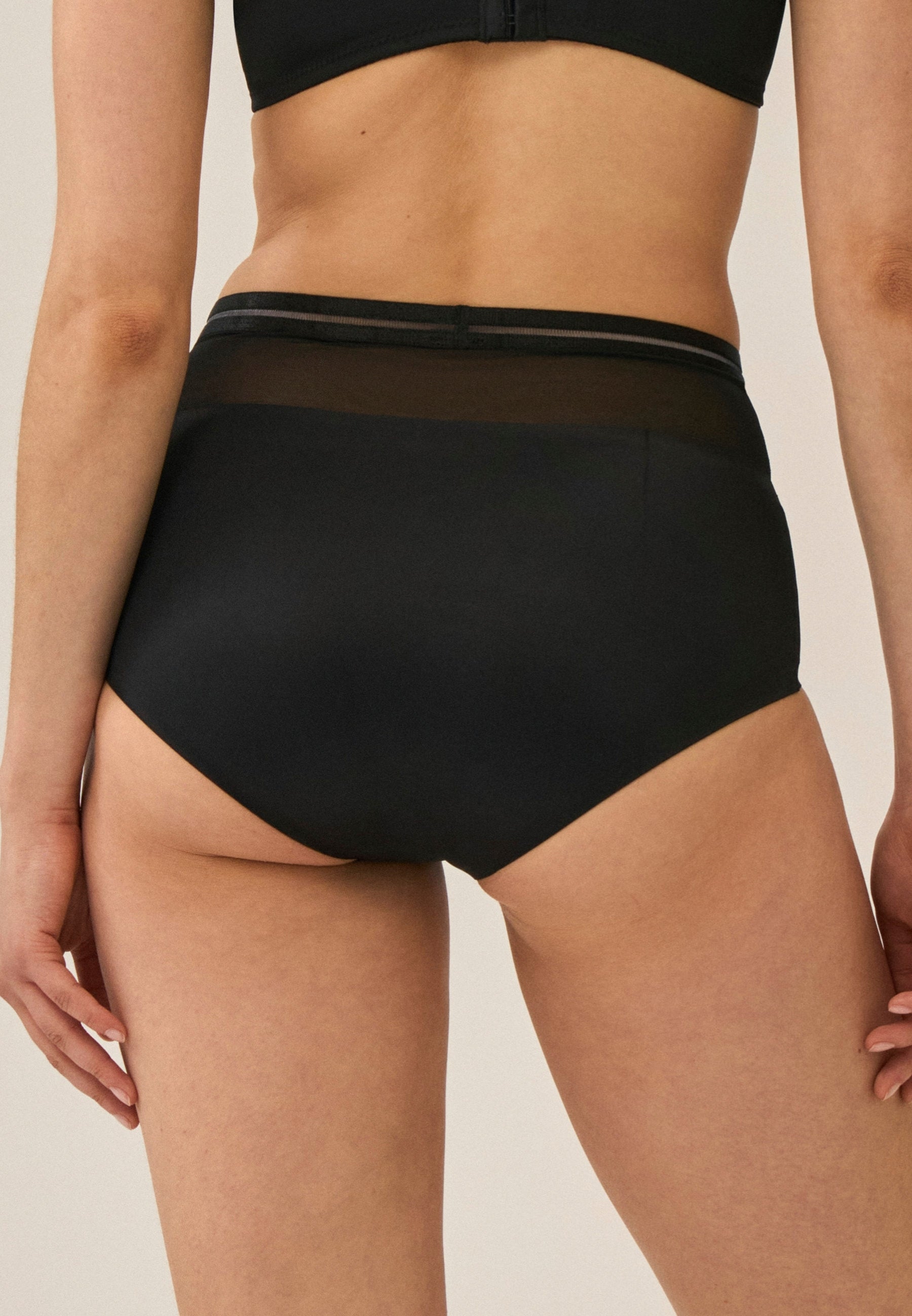 Achterzijde van vrouw die de hoge slip met mesh detail in de kleur zwart van het merk Naturana draagt