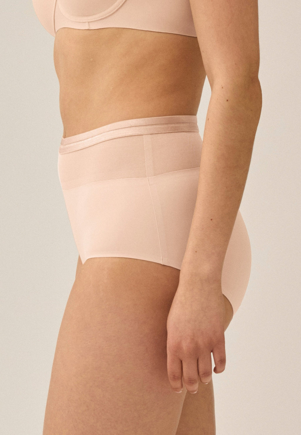 Zijde van vrouw die de hoge slip met mesh detail in de kleur beige van het merk Naturana draagt