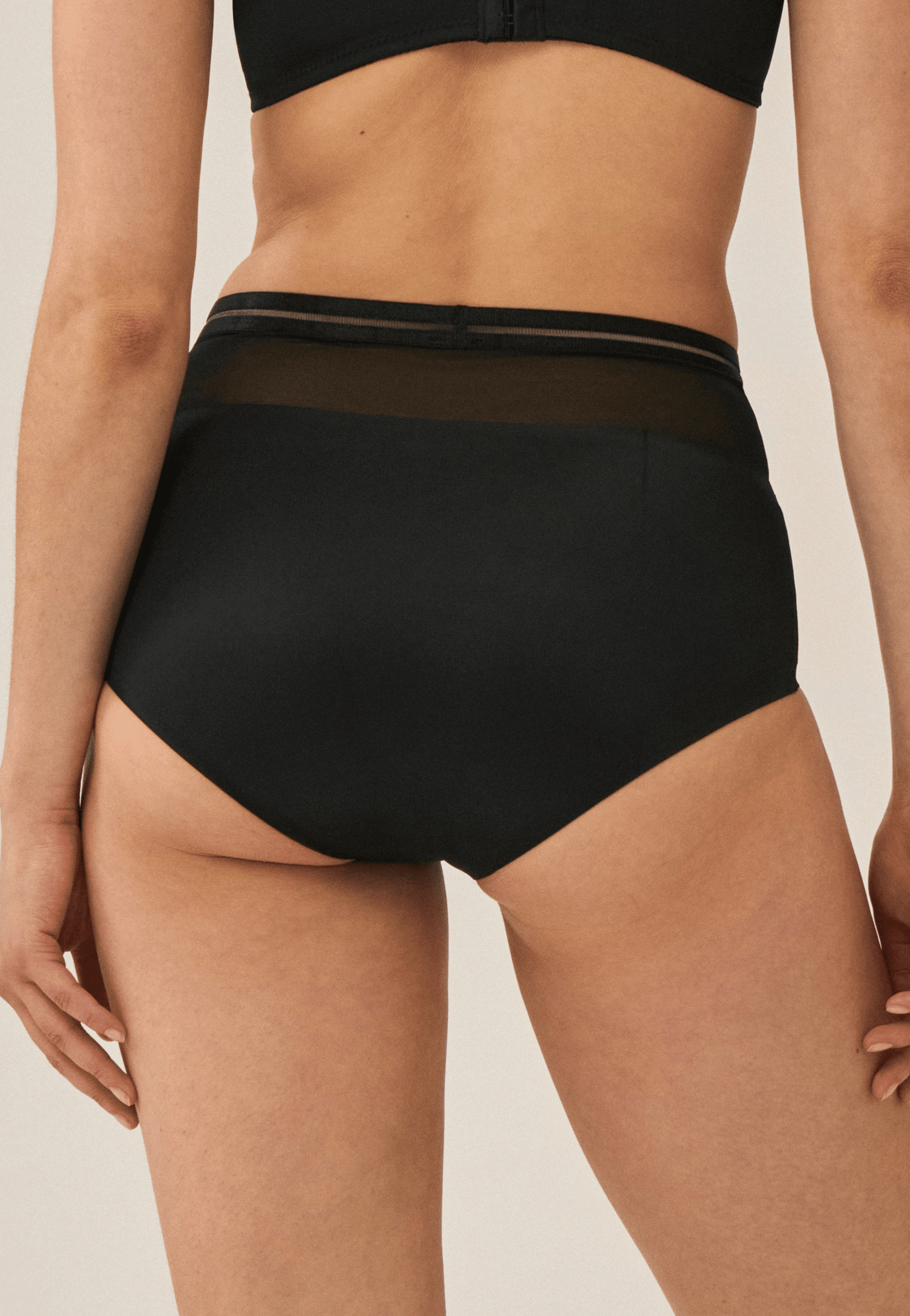 Achterzijde van vrouw die de hoge slip met mesh in de kleur zwart van het merk Naturana draagt