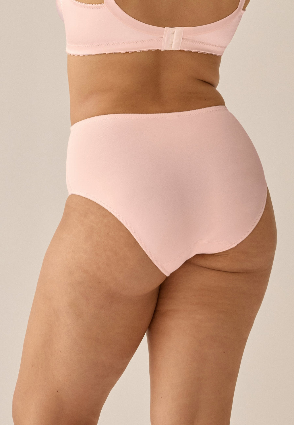 Achterzijde van vrouw die de minimizer slip met glanzend effect in de kleur blush van het merk Naturana draagt