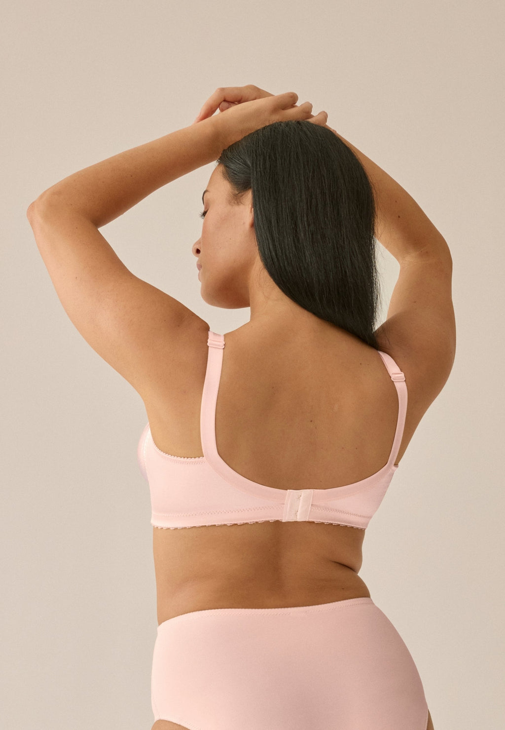 Achterzijde van vrouw die de minimizer bh met glanzend effect in de kleur blush van het merk Naturana draagt