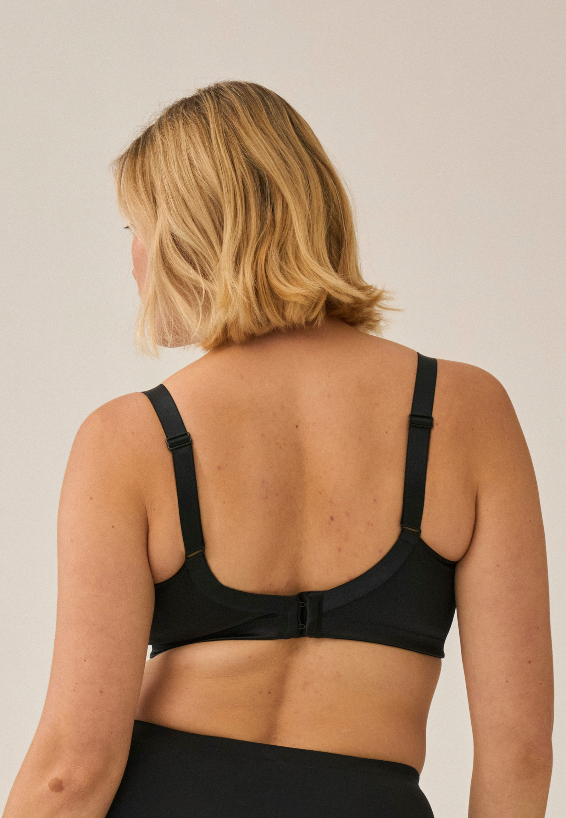 Achterzijde van vrouw die de minimizer bh met mesh detail in de kleur zwart van het merk Naturana draagt