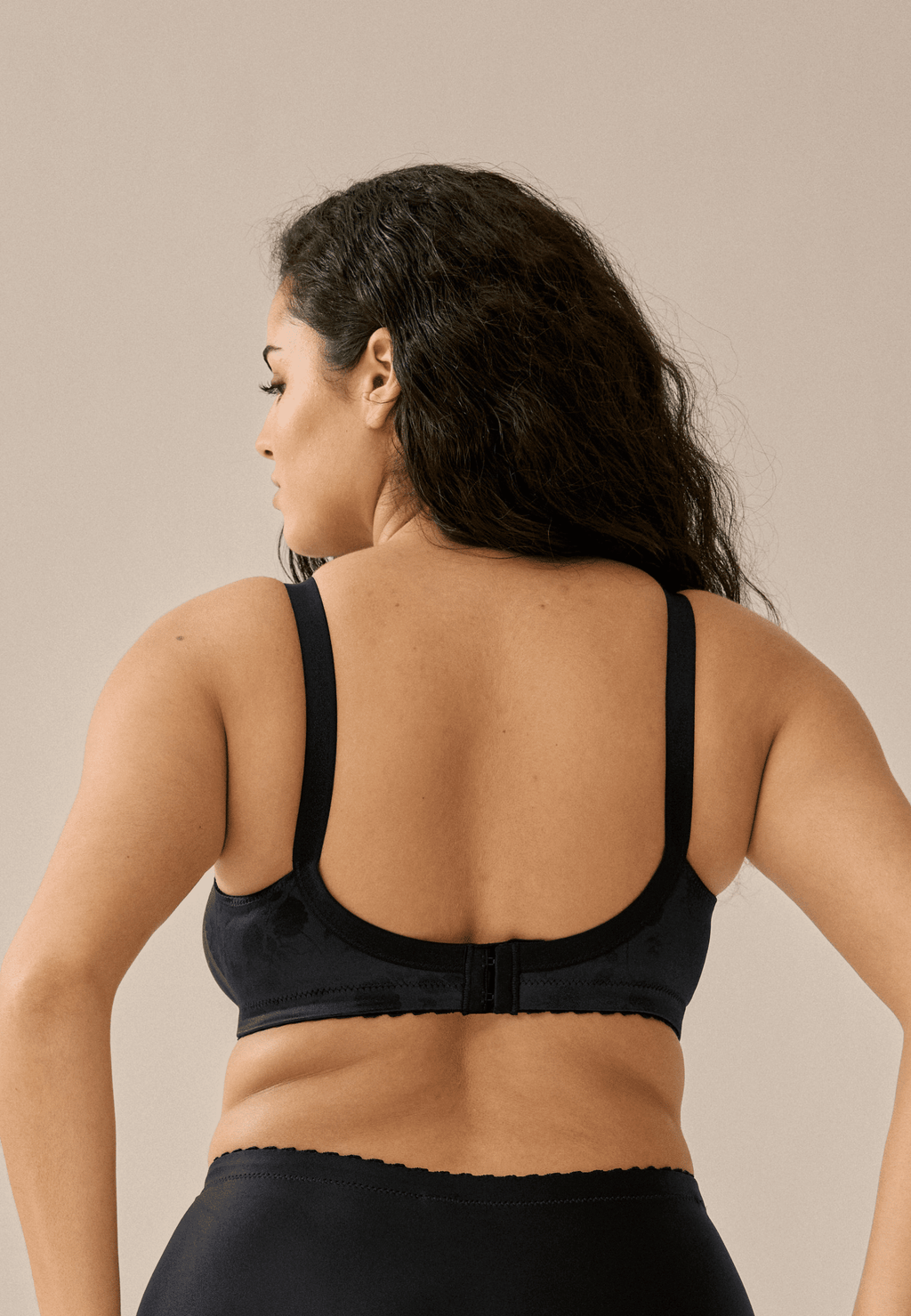 Achterzijde van vrouw die de minimizer bh met bloemenpatroon in de kleur zwart van het merk Naturana draagt
