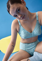 Voorzijde van vrouw die de minimizer bh en minimizer slip met bloemenpatroon in de kleur aquamarine van het merk Naturana draagt