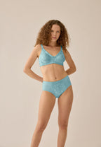 Voorzijde van vrouw die de minimizer bh en minimizer slip met bloemenpatroon in de kleur aquamarine van het merk Naturana draagt