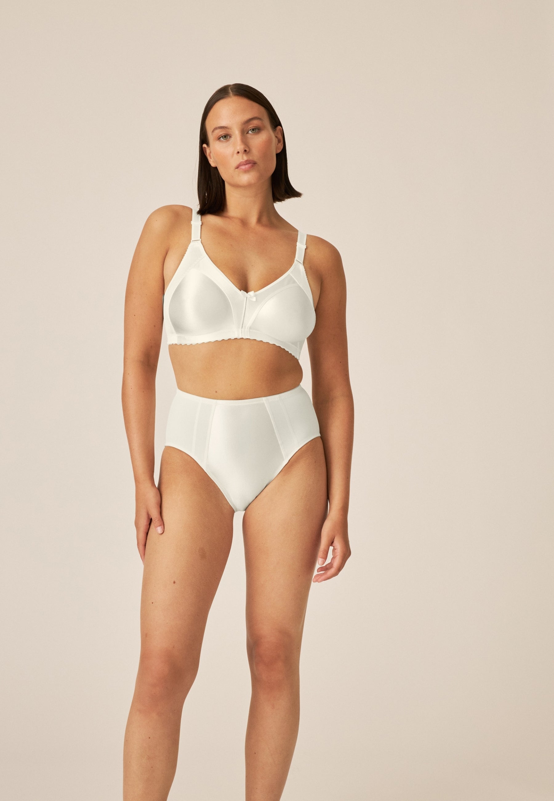 Zijde van vrouw die de minimizer bh en minimizer slip met glanzend effect in de kleur ivoor van het merk Naturana draagt