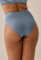 Achterzijde van vrouw die de minimizer slip met glanzend effect in de kleur moonlight blue van het merk Naturana draagt