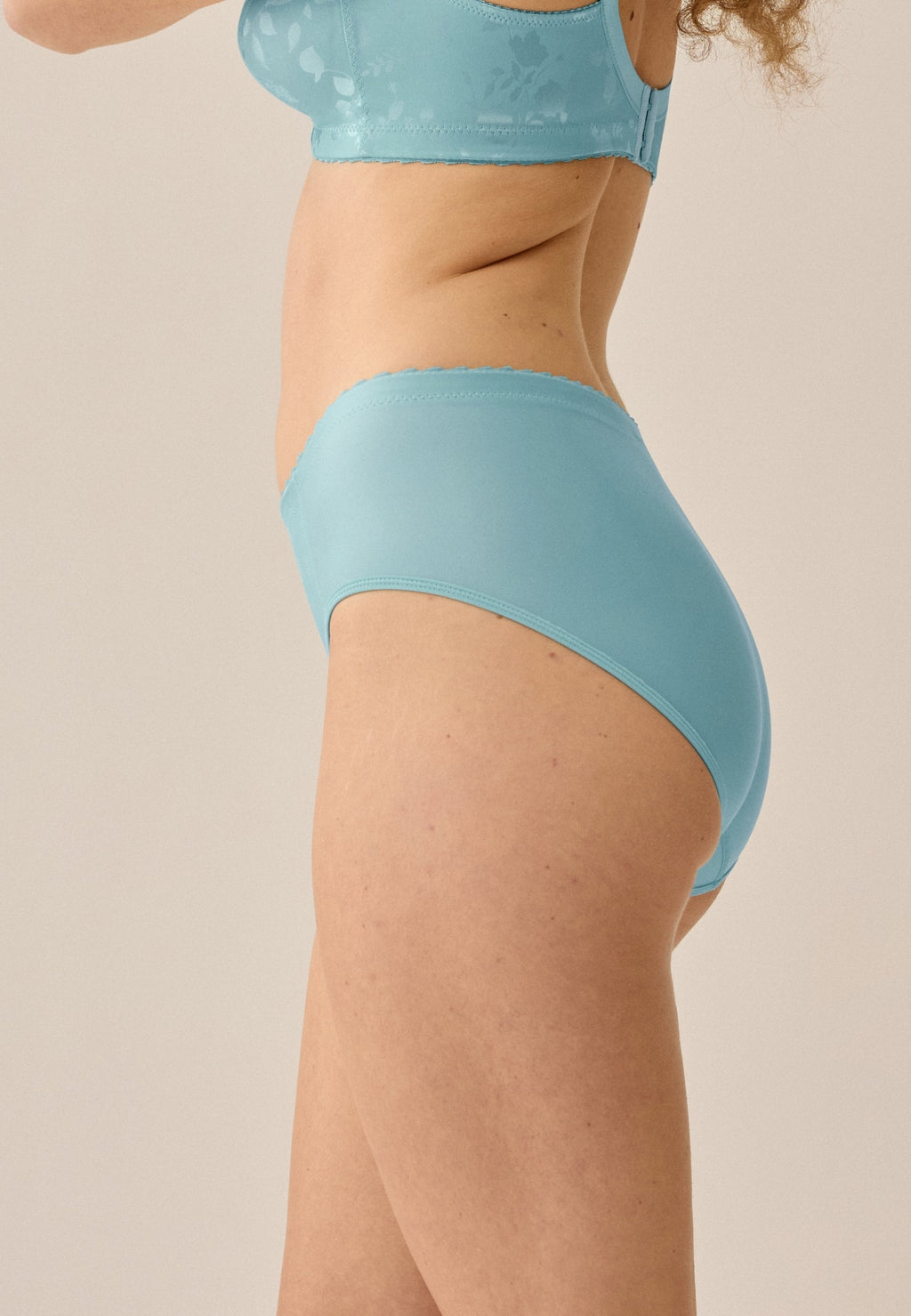 Zijde van vrouw die de minimizer slip met bloemenpatroon in de kleur aquamarine  van het merk Naturana draagt