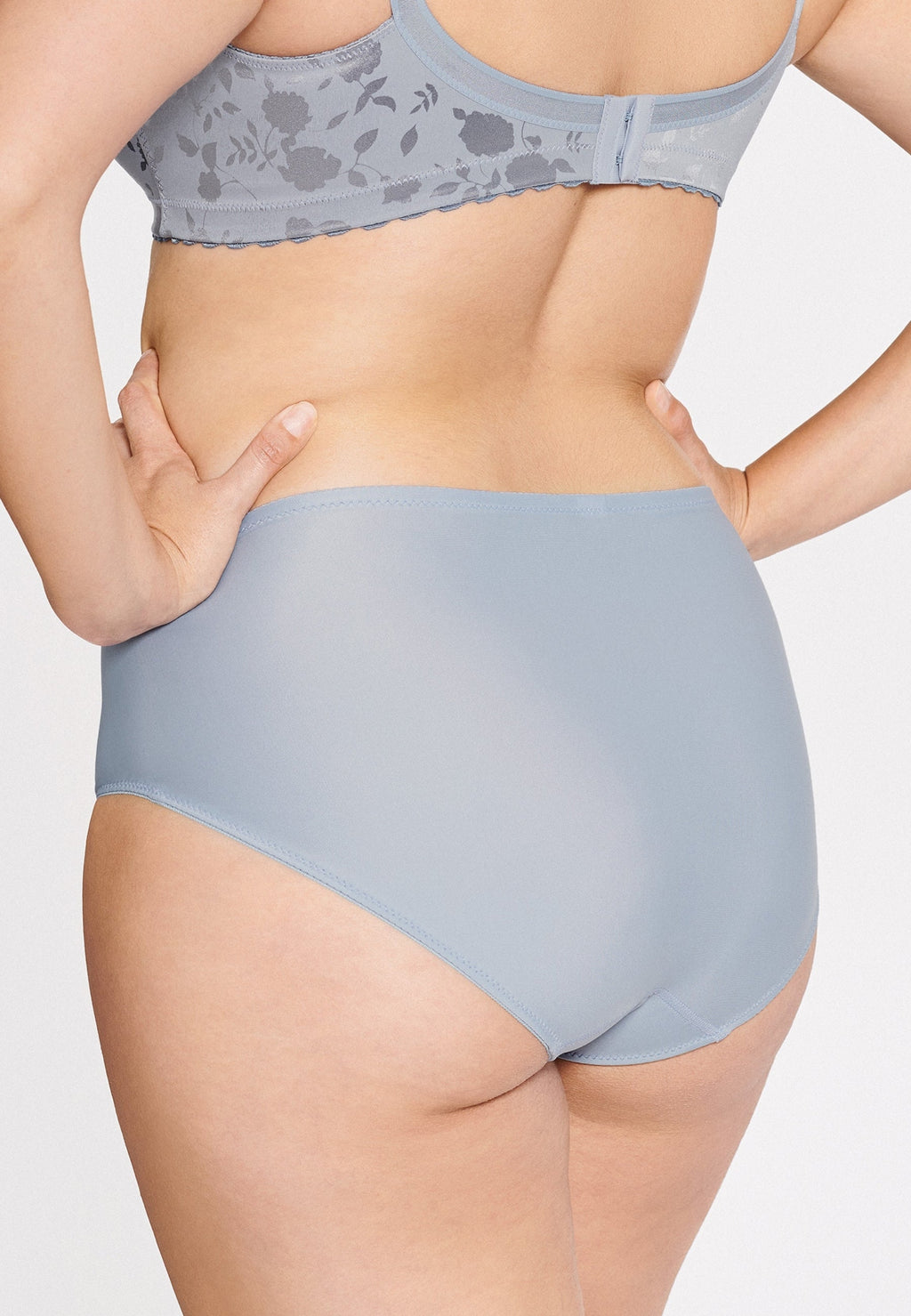 Achterzijde van vrouw die de minimizer slip met bloemenpatroon in de kleur raindrops van het merk Naturana draagt