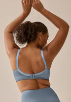 Achterzijde van vrouw die de minimizer bh met glanzend effect en minimizer slip in de kleur moonlight blue van het merk Naturana draagt