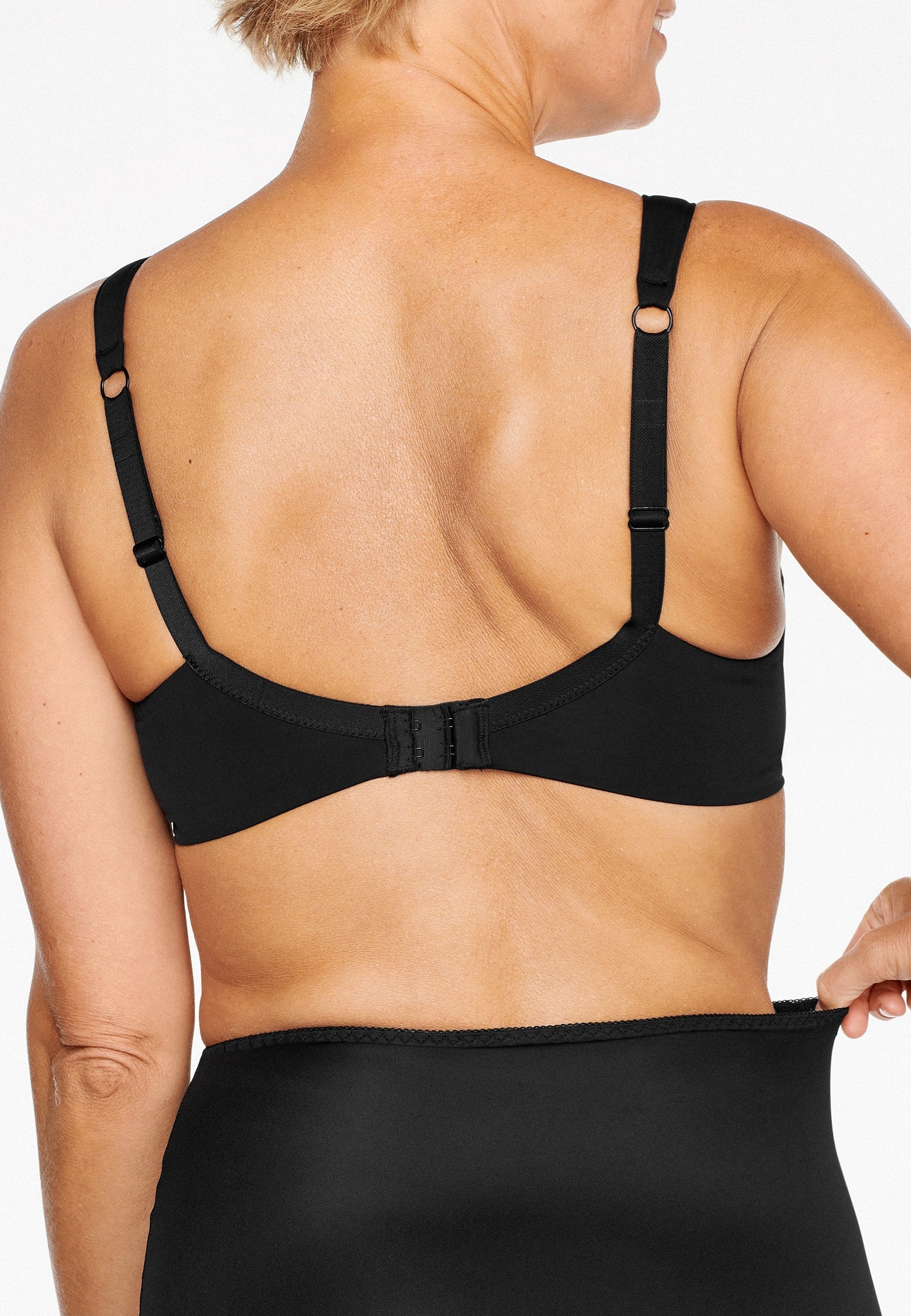 Achterzijde van vrouw die de soft bh met glansband in de kleur zwart van het merk Naturana draagt