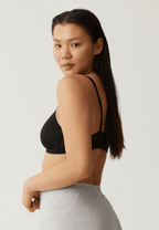 Zijde van vrouw die de soft bh met mesh bandjes in de kleur zwart van het merk Naturana draagt