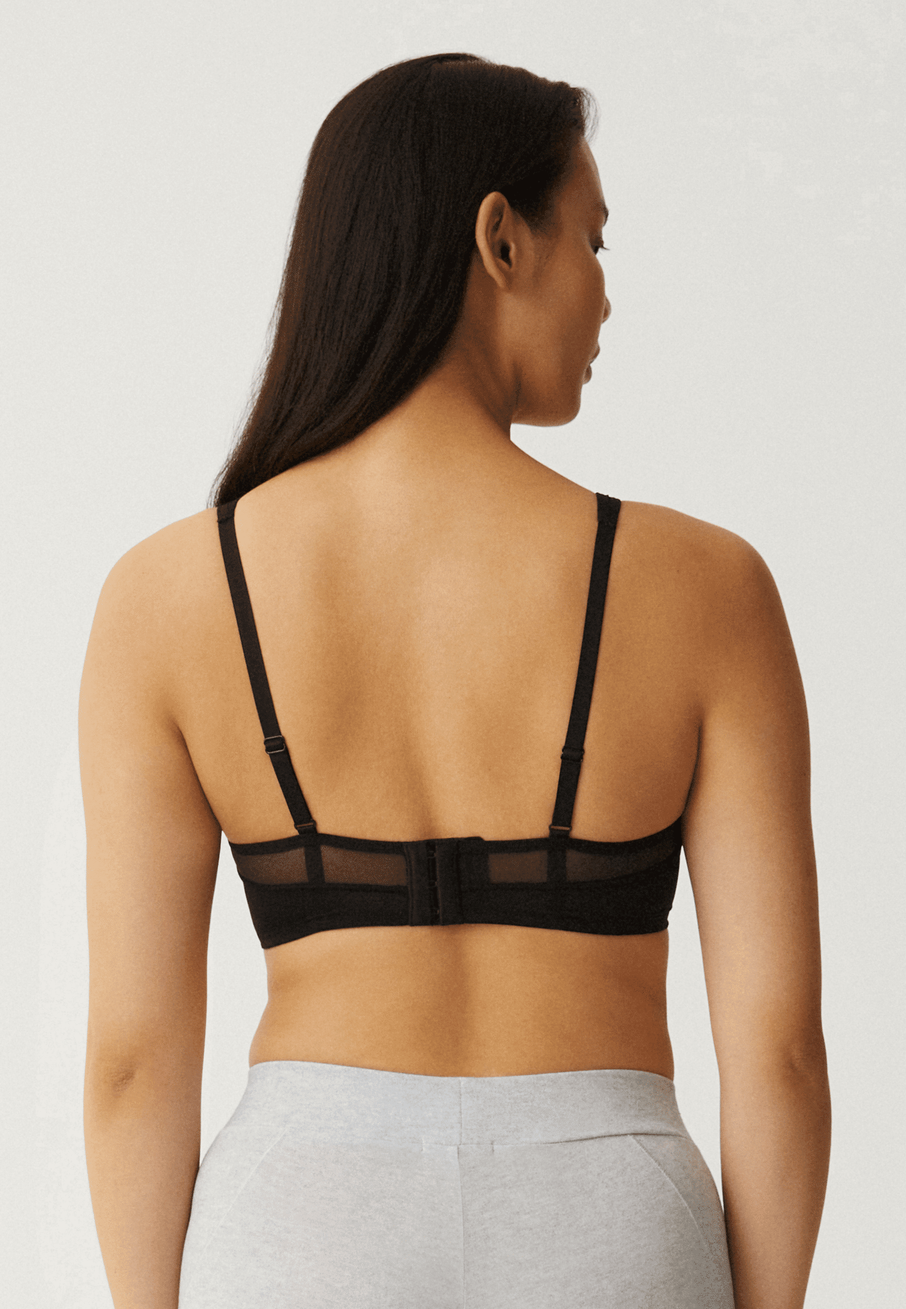 Achterzijde van vrouw die de soft bh met mesh bandjes in de kleur zwart van het merk Naturana draagt