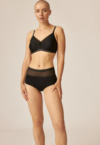 Voorzijde van vrouw die de soft bh met mesh detail en hoge slip met mesh detail n de kleur zwart van het merk Naturana draagt