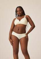 Voorzijde van vrouw die de soft bh met glansband en slip met glansband in de kleur ecru van het merk Naturana draagt