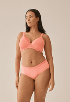 Voorzijde van vrouw die de soft bh met glansband en slip met glansband in de kleur peach pink van het merk Naturana draagt