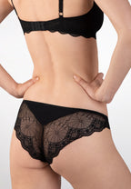 Achterzijde van vrouw die de tanga met kant in de kleur zwart van het merk Naturana draagt
